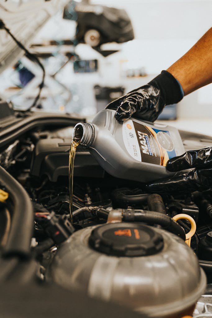 A close-up of a mechanic in gloves pouring engine oil into a car engine, showcasing automotive maintenance.thebaddieshub.com