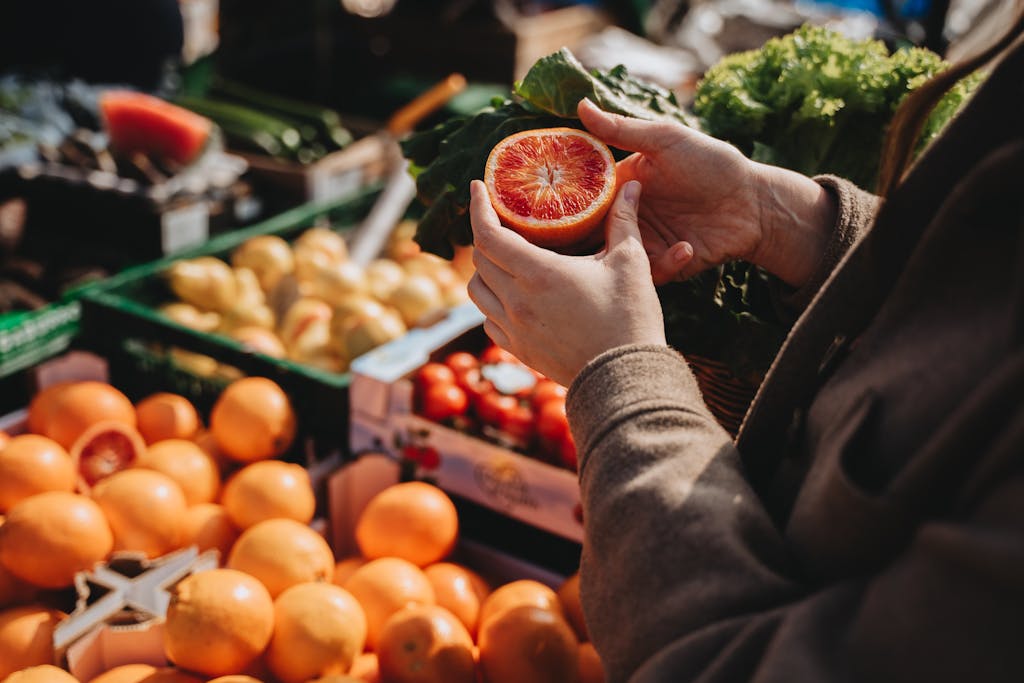 A close-up of a person VeganovTrichy holding a sliced orange at an outdoor market, showcasing fresh produce.