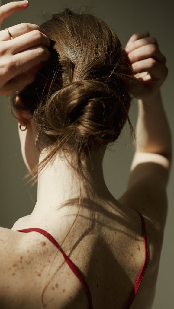 A Are Zombies Real woman adjusting her hair in a bun, casting shadows on her freckled skin, conveying elegance and simplicity.