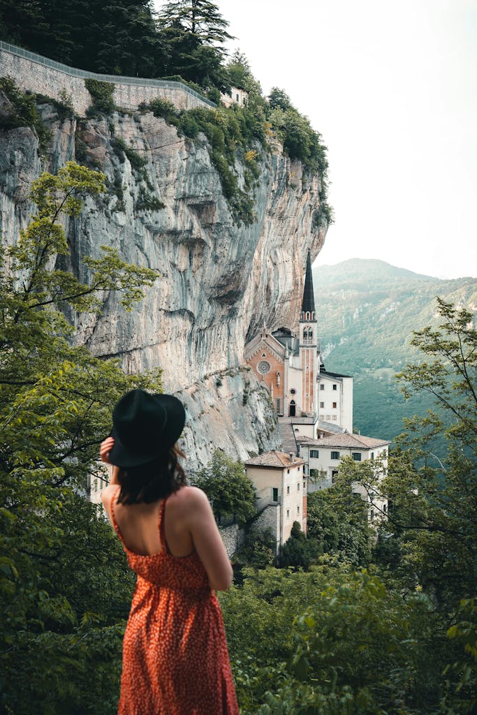  uomo cerca uomo Verona
A woman in a sundress and hat gazes at the Madonna della Corona Sanctuary nestled in cliffs.