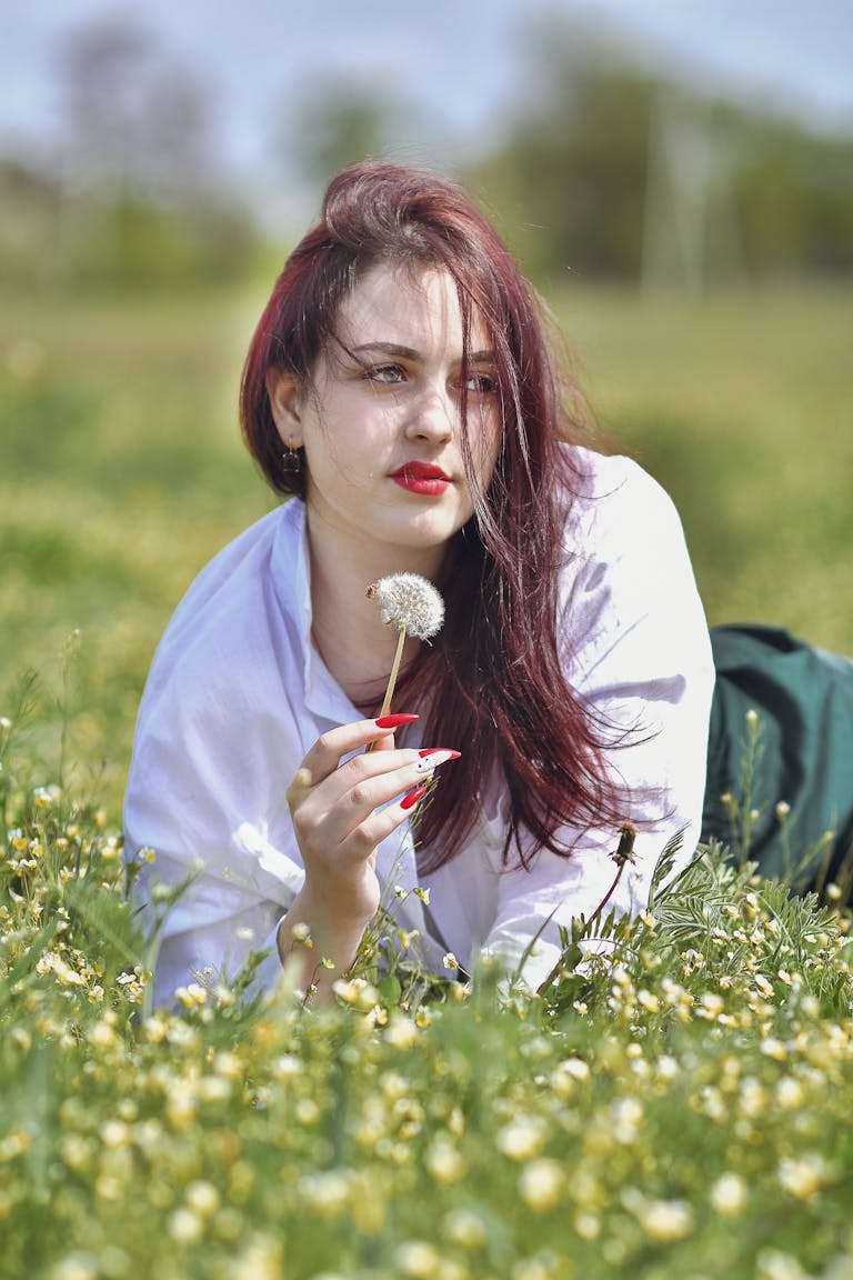 Pantagonar A woman lies in a field of flowers holding a dandelion during a sunny spring day.