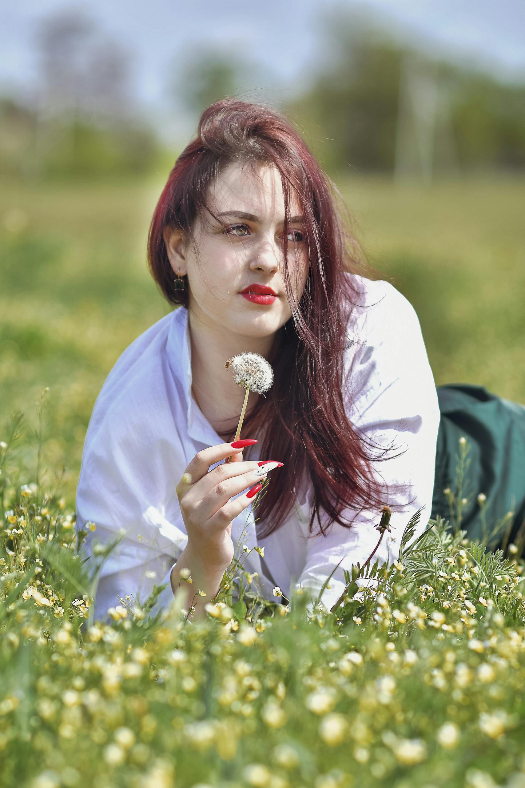 Pantagonar A woman lies in a field of flowers holding a dandelion during a sunny spring day.