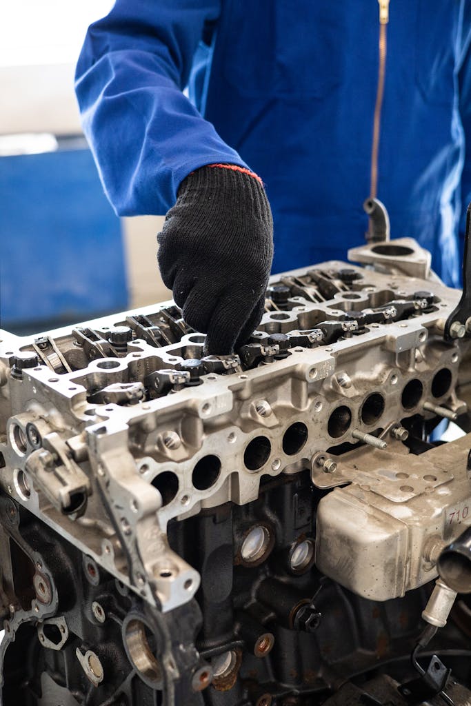 Close-up of a Car Mechanic Near Me in gloves working on a car engine cylinder head in a workshop setting.thebaddieshub.com