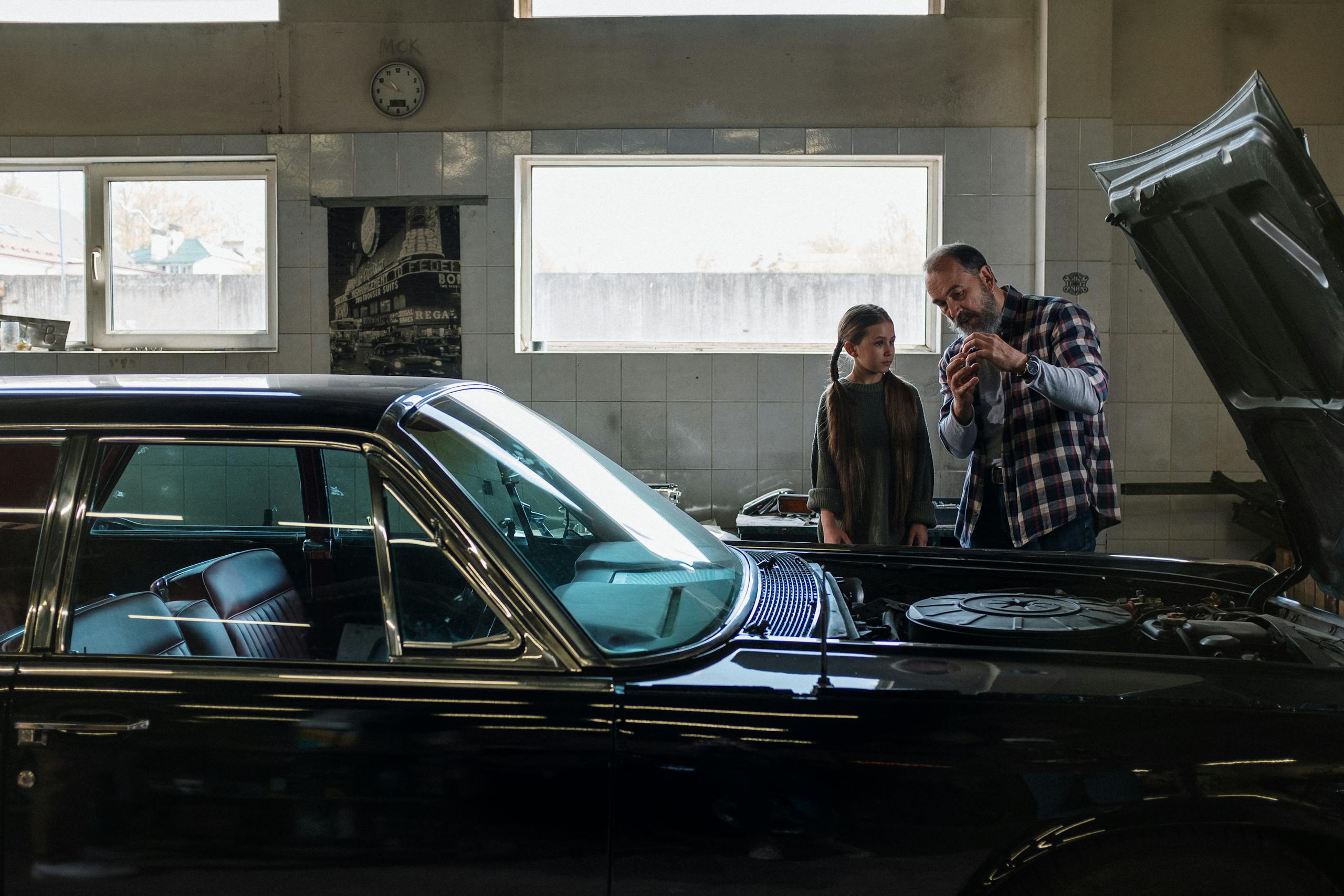 Father explains Car Mechanic Near Me to daughter in an auto repair shop. A moment of learning and bonding.thebaddieshub.com