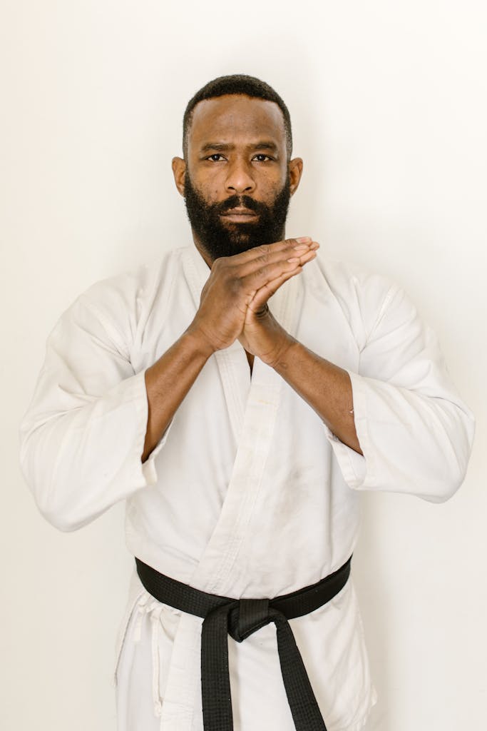 Panantukan DVDs Focused martial artist in white gi with black belt poses indoors, embodying discipline and strength.