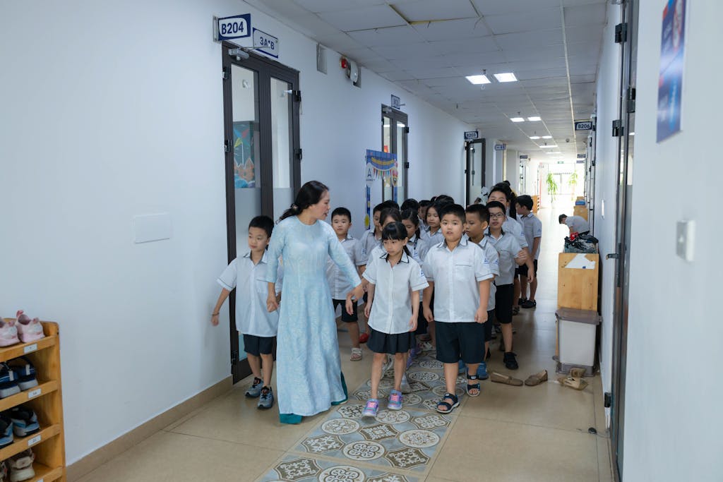 Classroom 15x Teacher guiding students in uniform through school corridor.