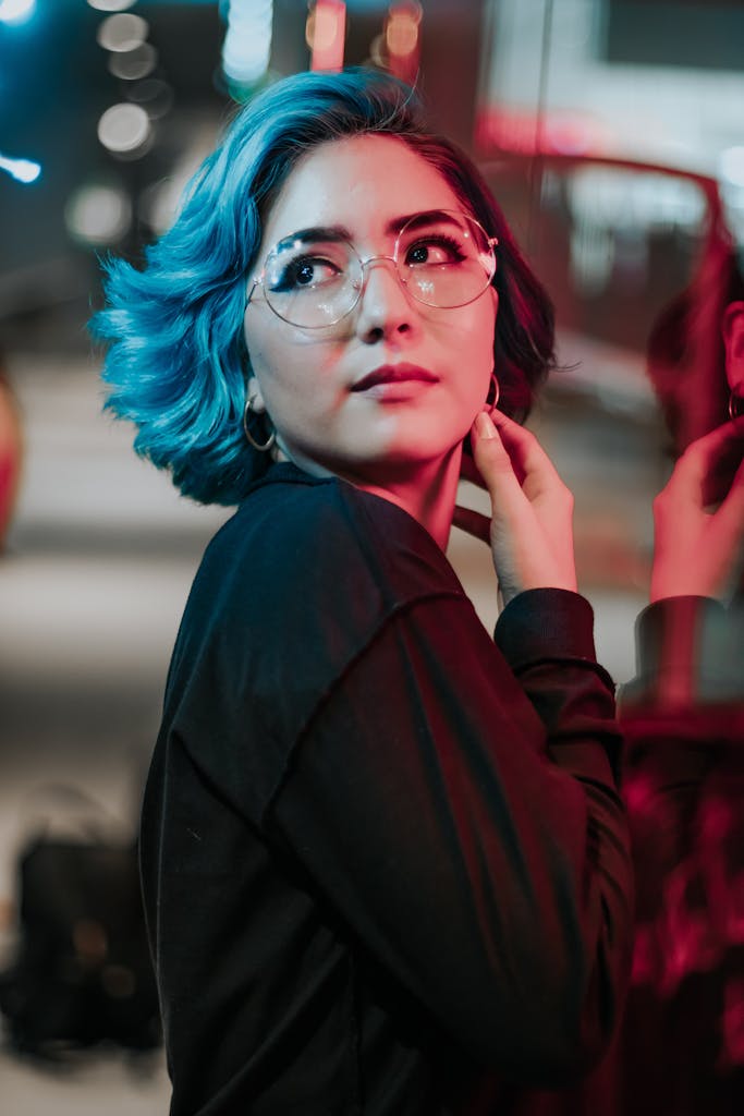 Shihuanuo Vibrant portrait of an Asian woman with blue hair and glasses under colorful city lights.