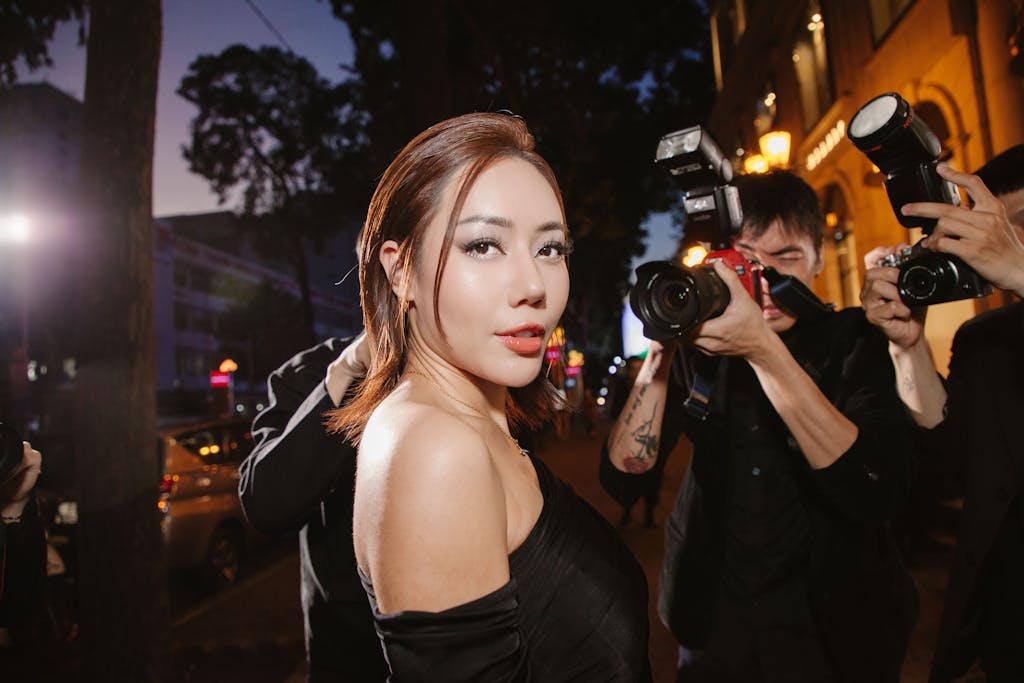 Influencers Gone Wild A glamorous woman in black poses confidently for photographers at a night event.
