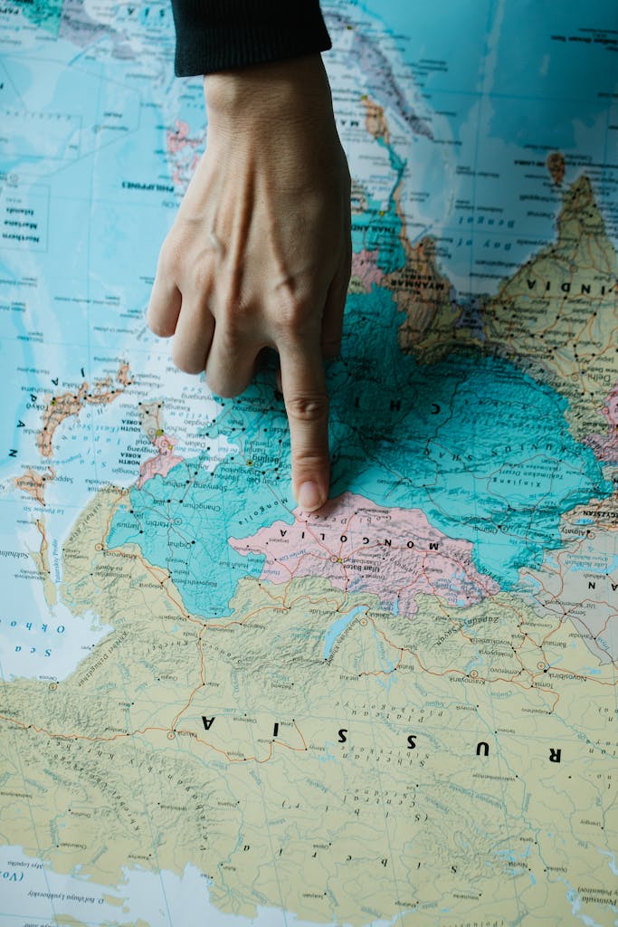 A hand points at Mongolia on a geographical map, showcasing geography and location details.