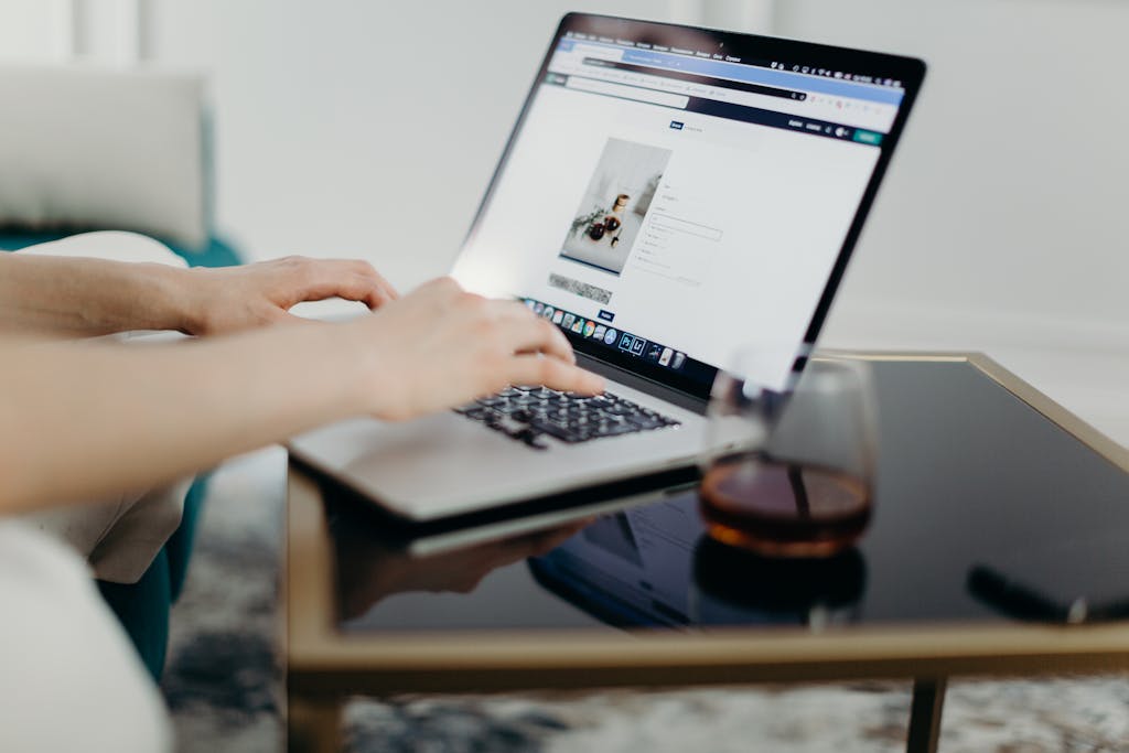 Uploadblog.com  A person typing on a laptop in a stylish home office with a glass of drink nearby.