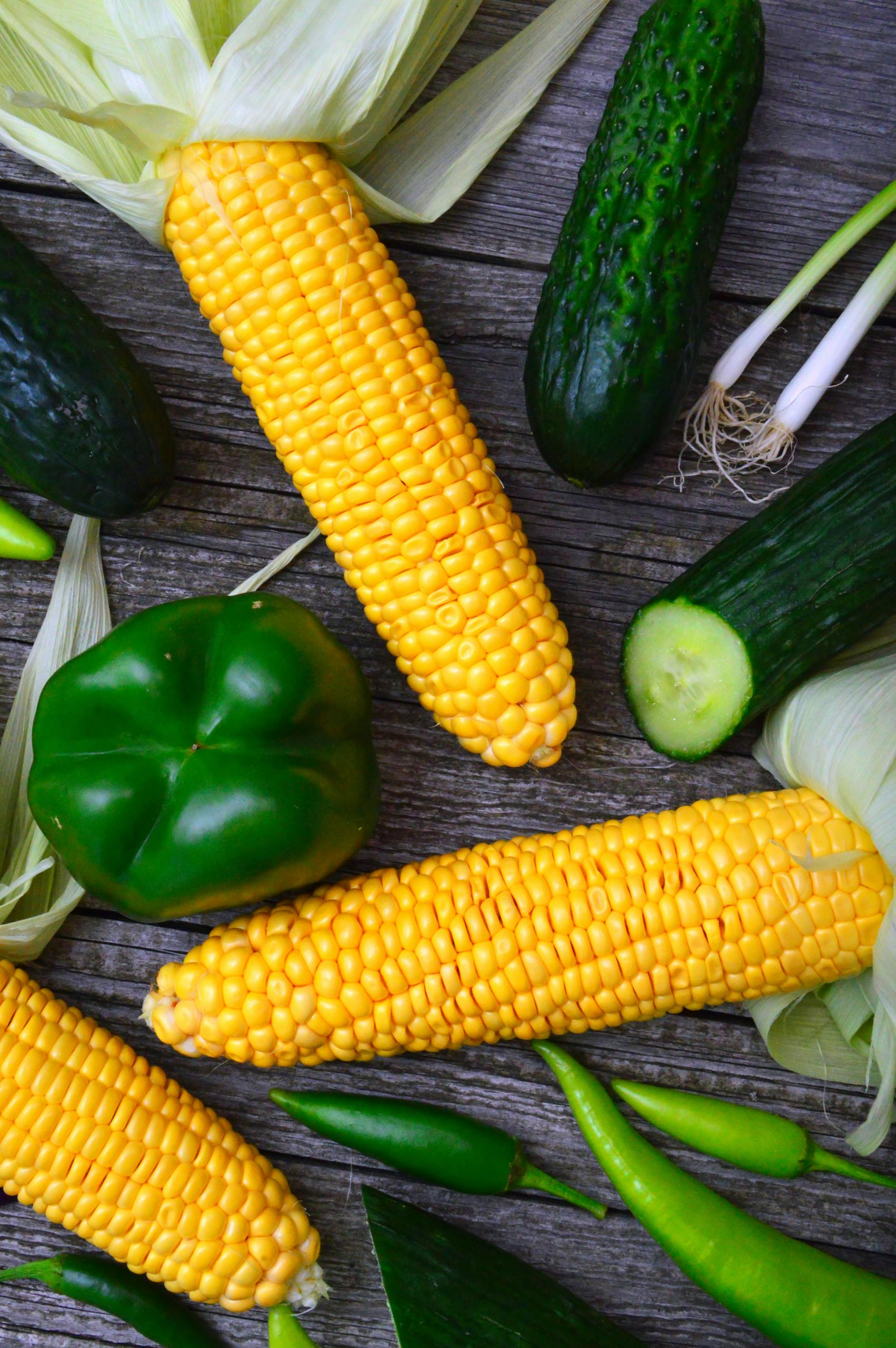A vibrant assortment of fresh , Canning Corn peppers, and cucumbers on a wooden table.