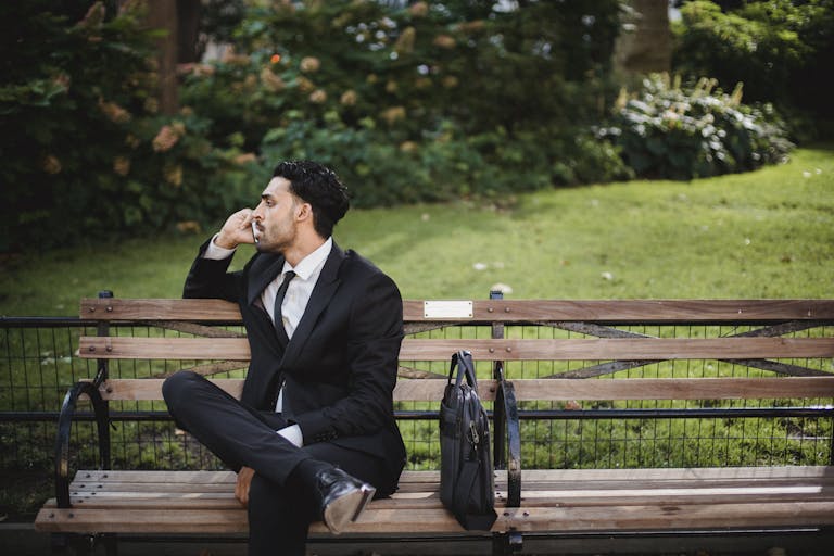 Smart Finance Tips and Updates for 2025 A well-dressed man in a black suit sits on a park bench talking on the phone.