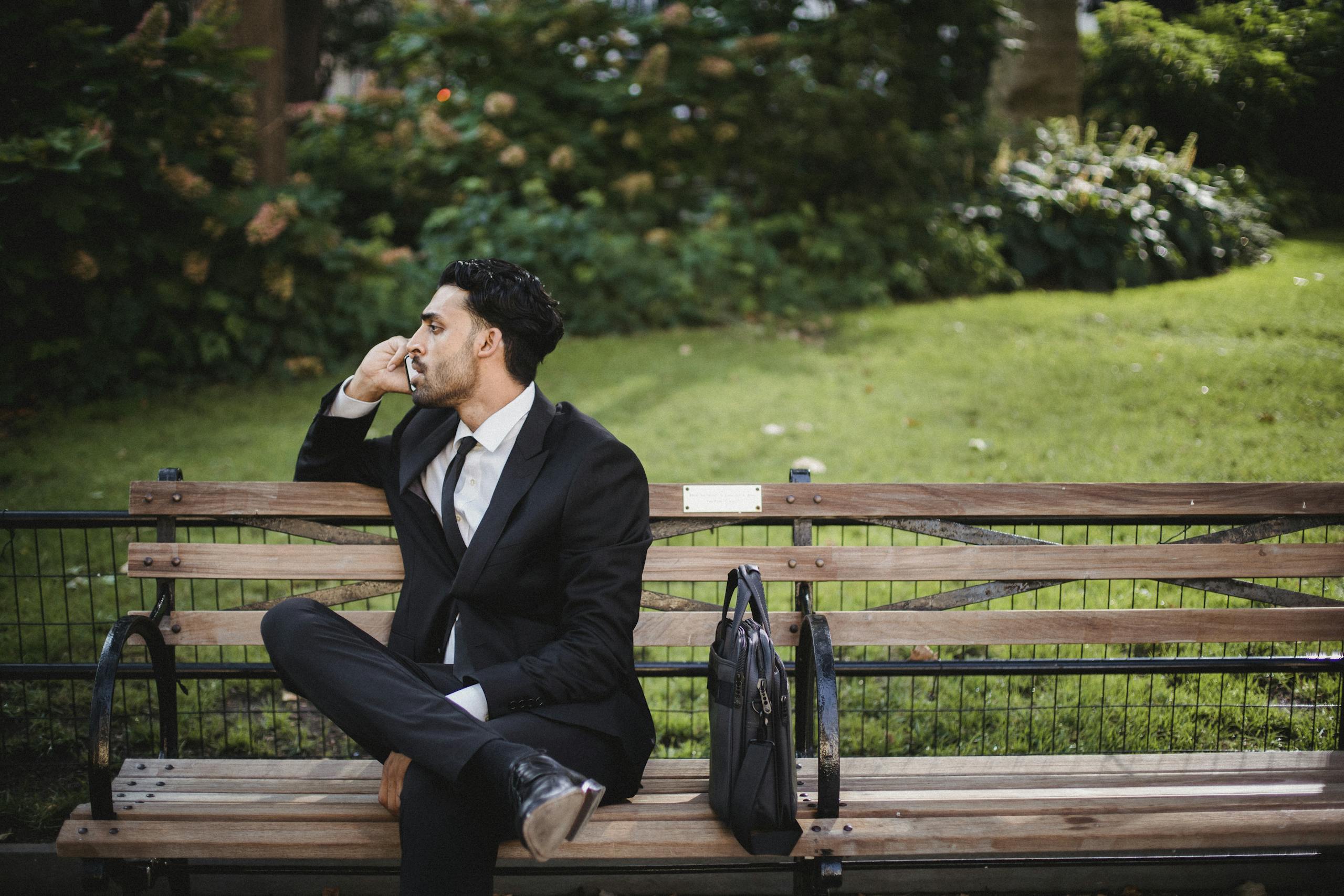 Smart Finance Tips and Updates for 2025 A well-dressed man in a black suit sits on a park bench talking on the phone.