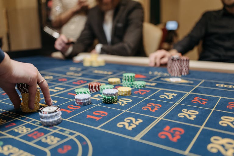 Hands placing betting 277bet.com chips on a roulette table in an upscale casino setting.