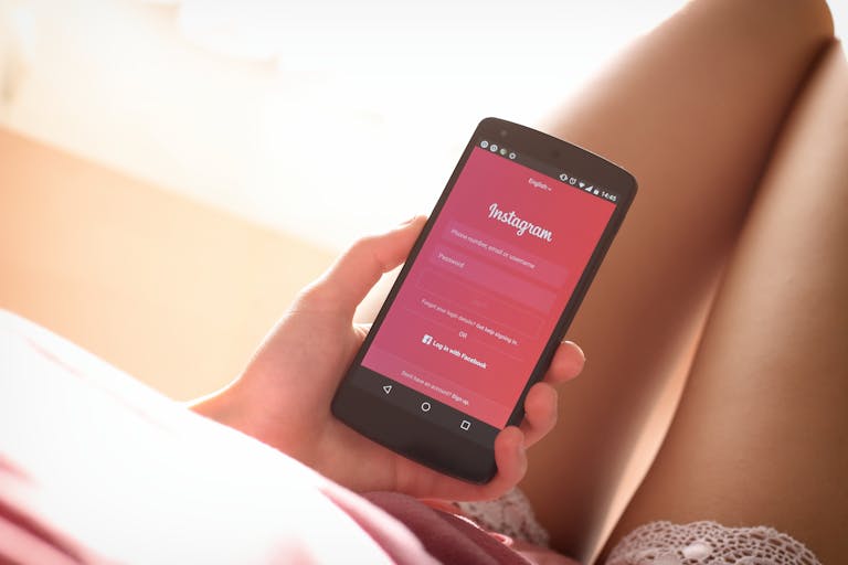 Maligoshik Leaks Woman holding a smartphone with Instagram login screen while relaxing indoors.