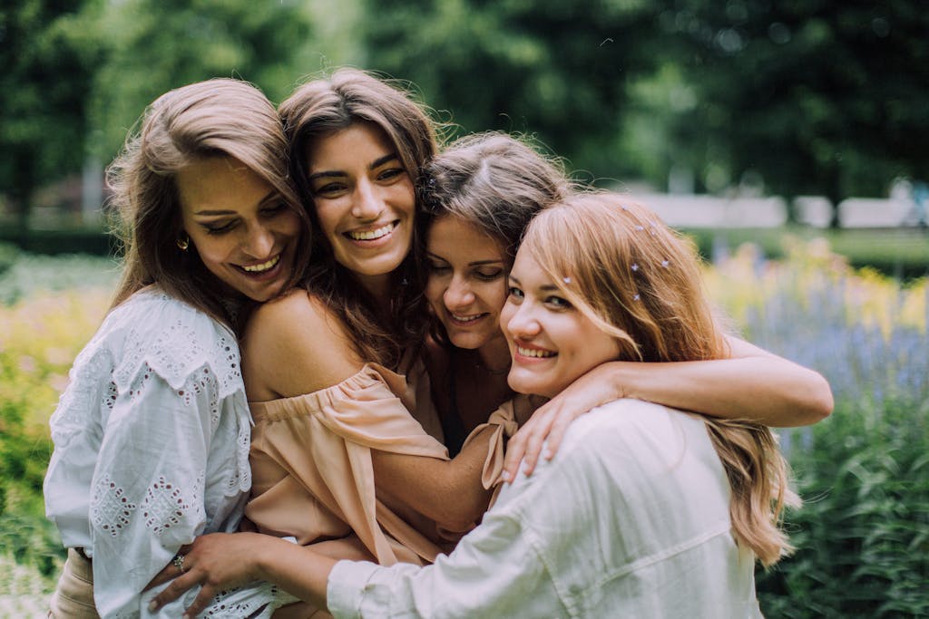 Four smiling women joyfully embrace in a lush green park during summer, showcasing genuine friendship and happiness.