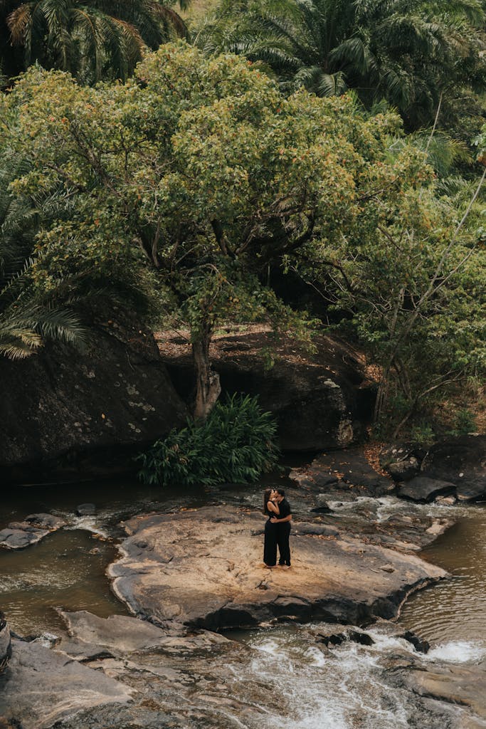  Simpciyu Romantic couple embracing on a rocky river island surrounded by lush green forest.