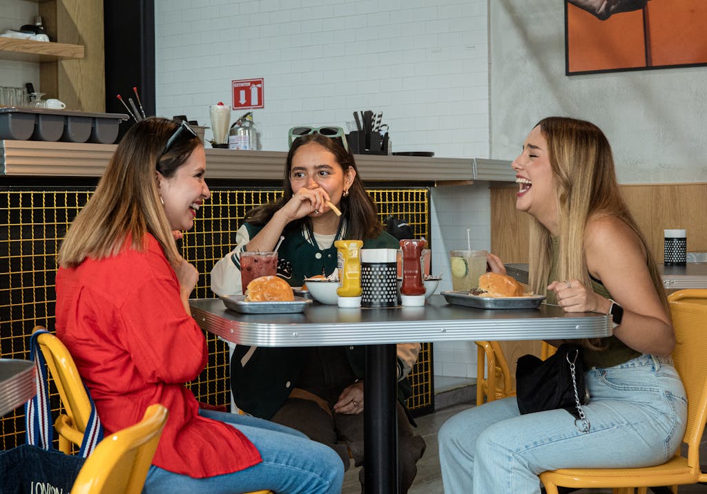 Yalla Choy Three friends laughing and enjoying burgers in a vibrant city cafe.