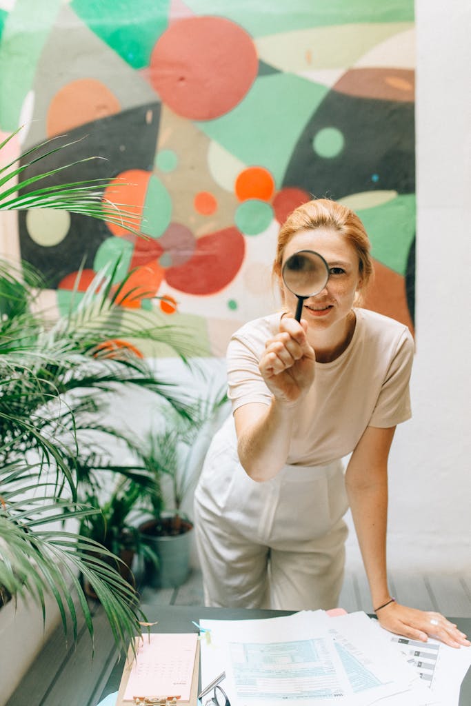 SONE 248 Young woman using magnifying glass to examine documents in a bright, artistic indoor setting.