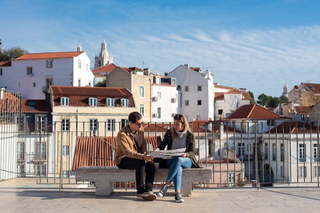 Kirby Dedo A couple sitting on a bench looking at a map with Lisbon's rooftops in the background.