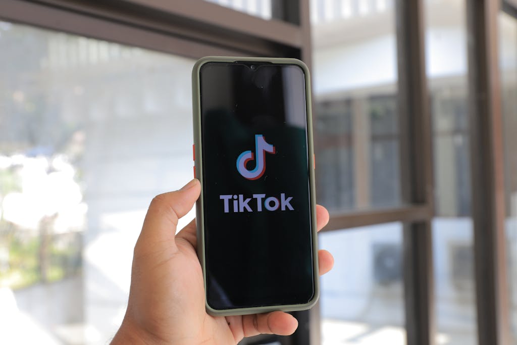 BaddiesOnly: Digital Culture, Branding, and the Rise of Online Communities A hand holds a smartphone displaying the TikTok app in an indoor setting.