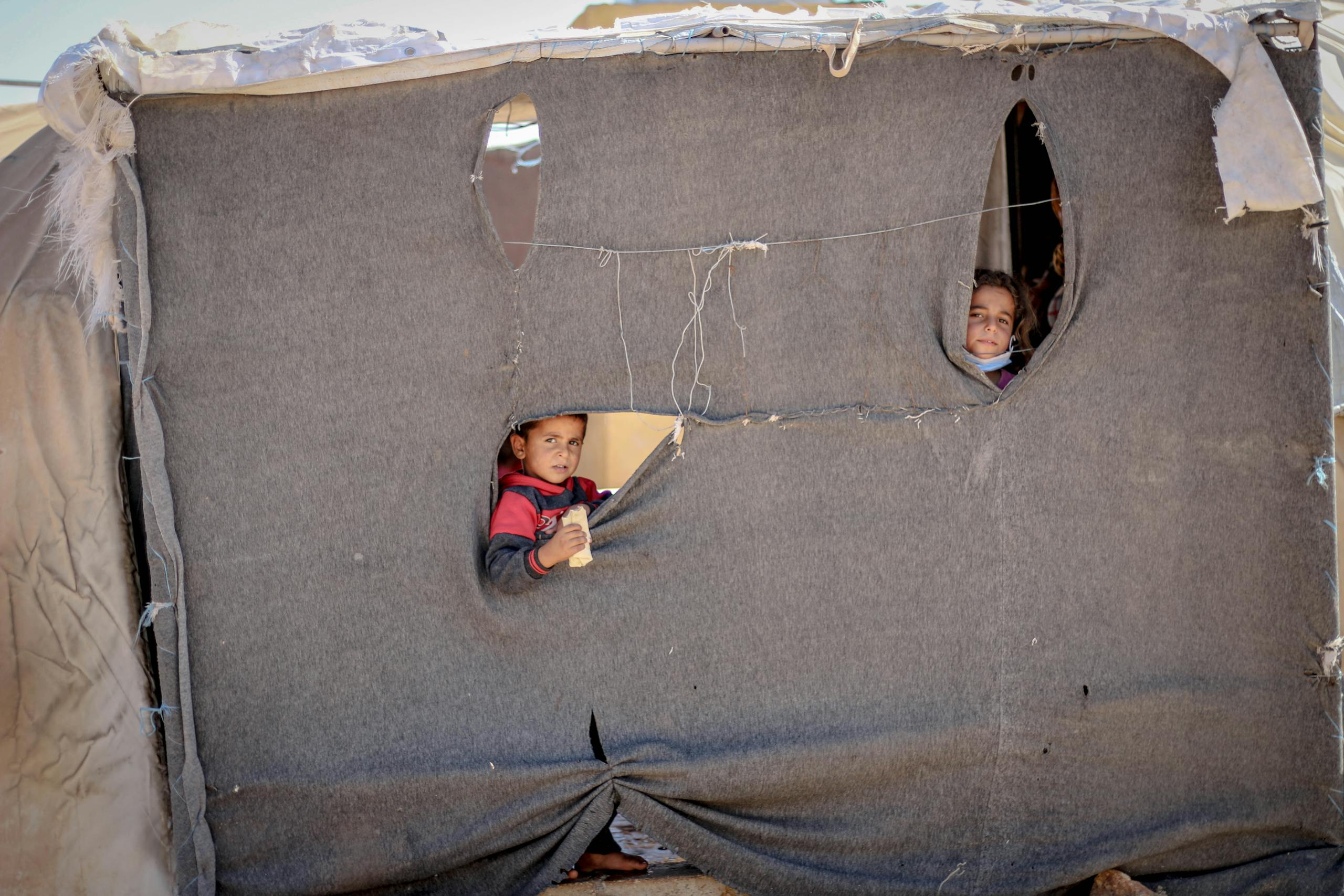 World War 2 Log: Children peeking through a makeshift tent in Idlib, highlighting resilience and hope.