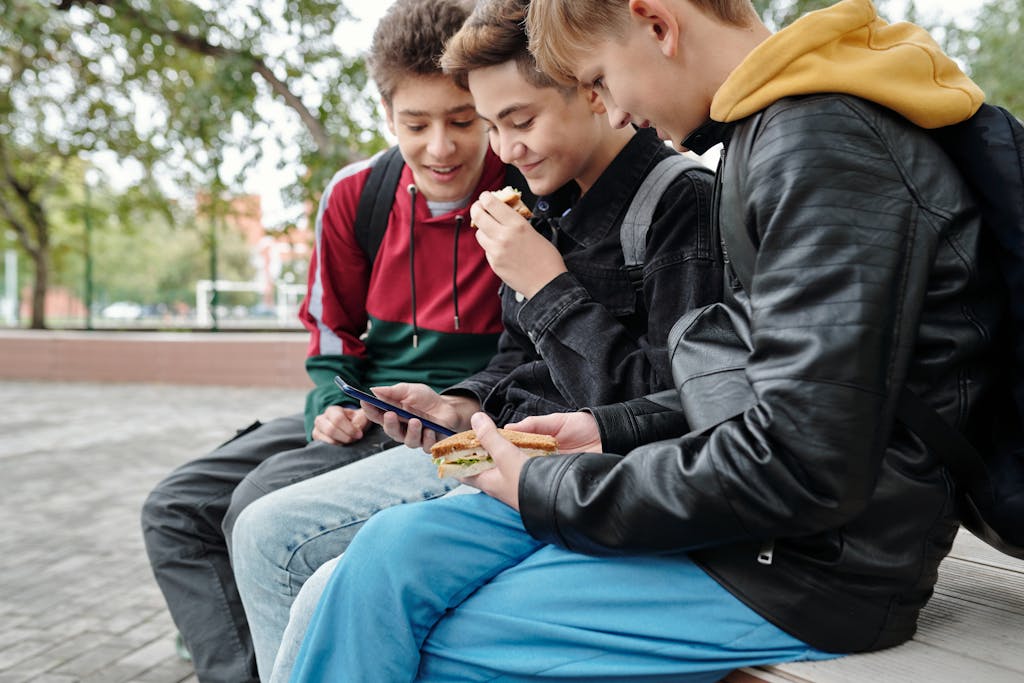 Australian Buddies Three teenage friends sitting outdoors, enjoying snacks and sharing a smartphone, enjoying their time together.