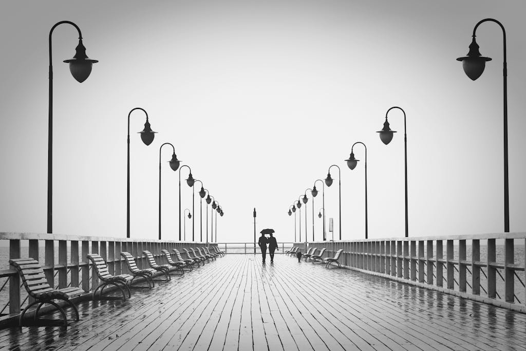 Sodiceram A couple holding umbrellas walks on a rainy boardwalk, embodying romance and tranquility.