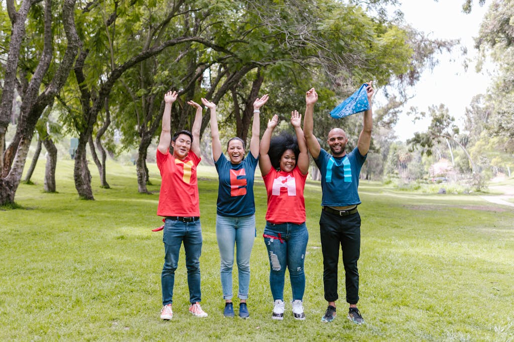 Juntosseguros A joyful group of diverse adults celebrating teamwork outdoors in a lush, green park.