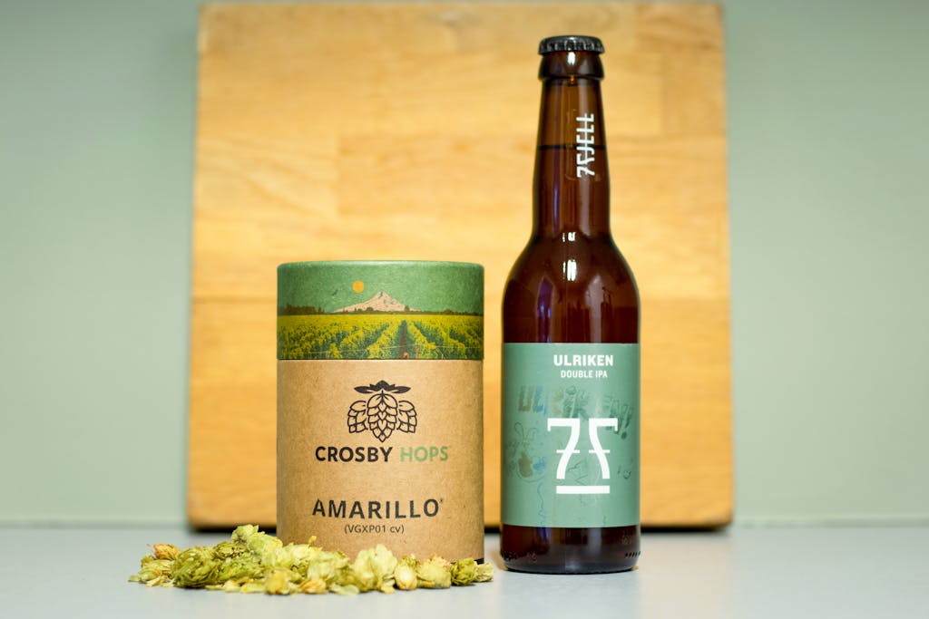 Nueraji vs Crosbie Prediction Beer bottle and Crosby Hops packaging with hops on table.