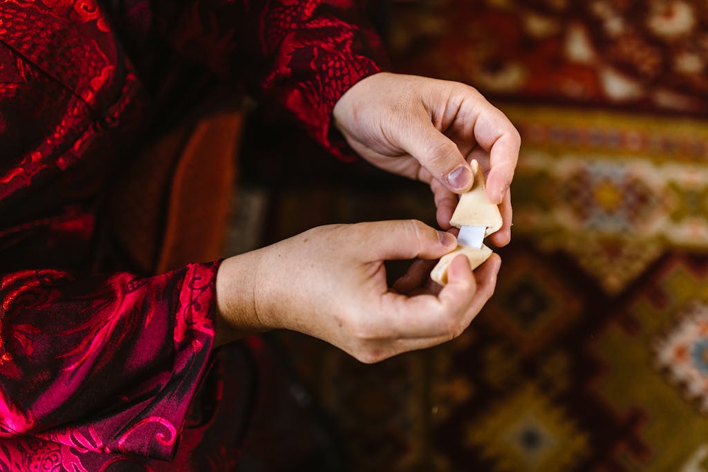 Nueraji vs Crosbie Prediction Close-up of hands opening a fortune cookie, dressed in ornate red fabric.