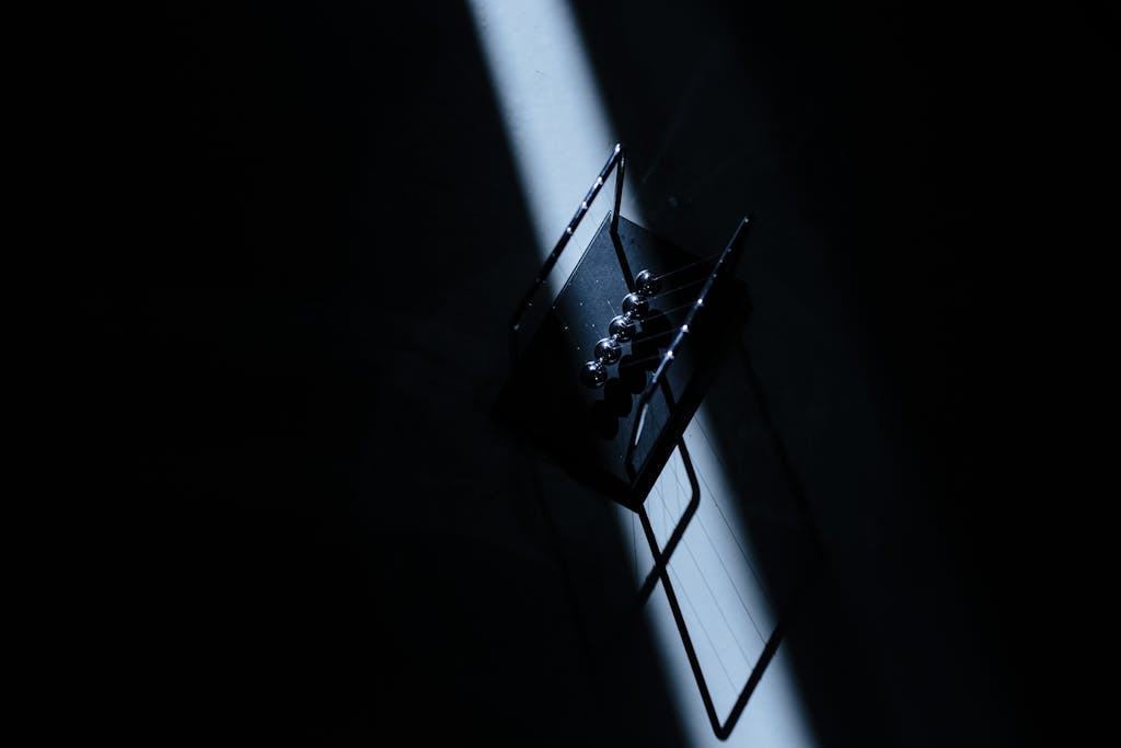 permanentad Newton's cradle in a dark room with striking light, showcasing physics concepts.